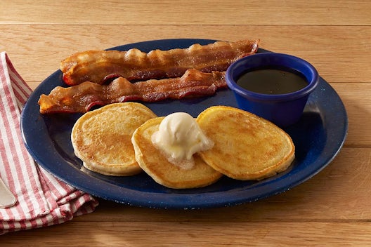 Mini buttermilk pancakes served with syrup, butter, and a side of bacon or sausage.